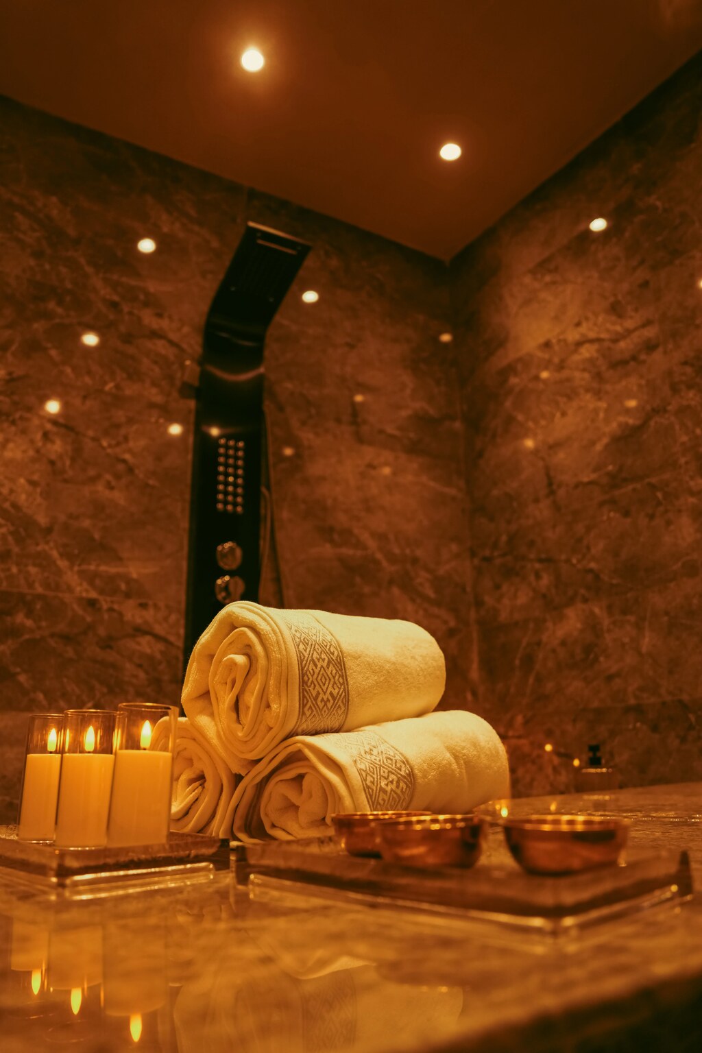 Luxury spa shower area with rolled towels, candles, and copper bowls on marble at Ellé Égante Spa